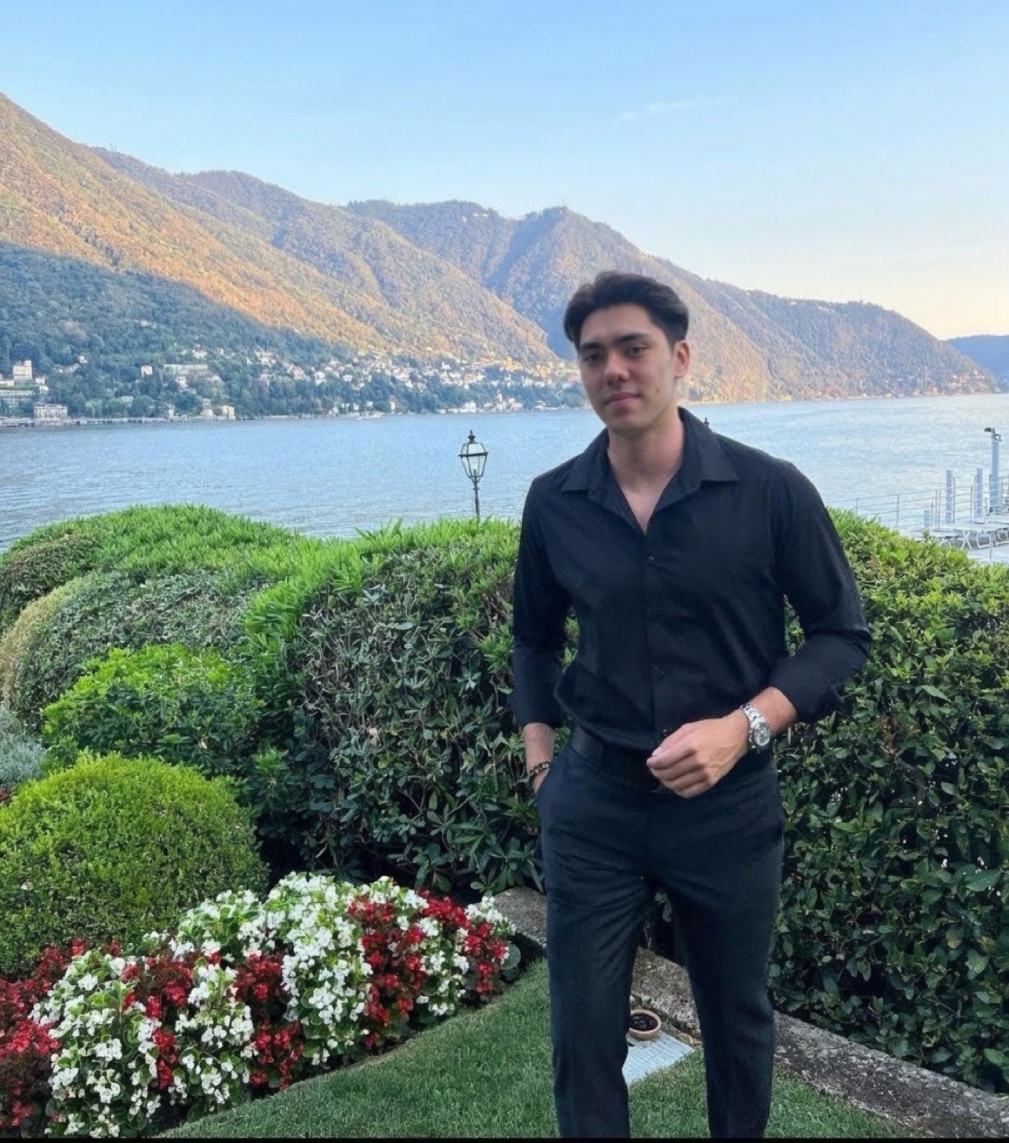 Matthew Stevens in a black shirt above a lake, with mountains and flower beds behind
