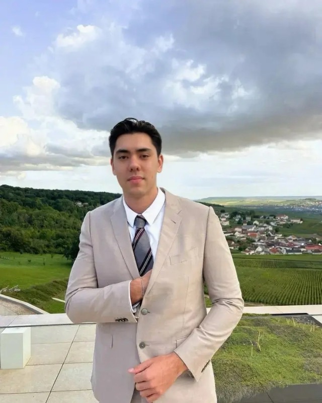 Matthew Stevens in a light beige suit and tie on a terrace above a green valley