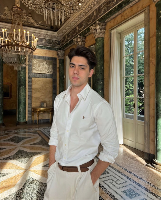 Matthew Stevens in a white shirt, hands in pockets, in an ornate gilded hall with a chandelier