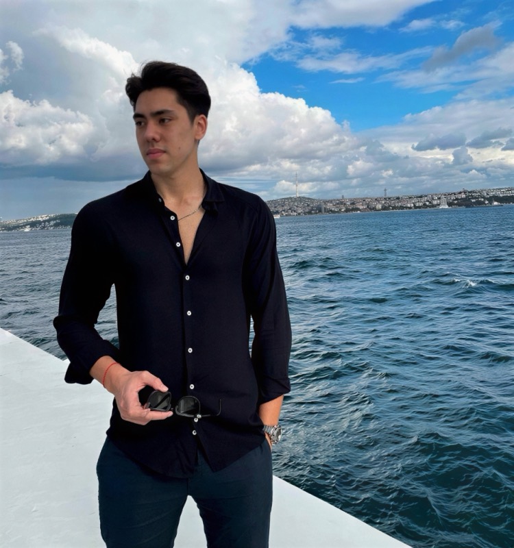 Matthew Stevens in a black shirt on a boat deck, with deep blue sea and big clouds behind