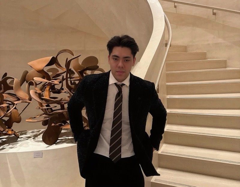 Matthew Stevens in a dark suit and striped tie beside a sweeping cream staircase